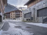 an old street in the mountains with cars parked in it under snow and some buildings