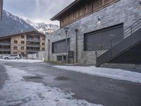 an old street in the mountains with cars parked in it under snow and some buildings