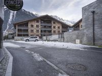 an old street in the mountains with cars parked in it under snow and some buildings