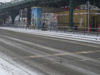 there is a man riding a bike down the road under a bridge in heavy snow