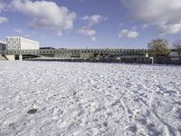 a large, snow covered field with some buildings and water fountains near it in the distance