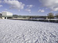 a large, snow covered field with some buildings and water fountains near it in the distance