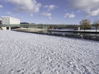 a large, snow covered field with some buildings and water fountains near it in the distance