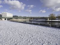 a large, snow covered field with some buildings and water fountains near it in the distance