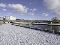 a large, snow covered field with some buildings and water fountains near it in the distance