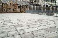 concrete patio with columns and fenced in area near building, during winter time, with trees, bushes and street lighting