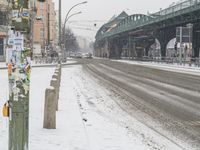 cars driving on a snow covered street in a city with a bridge above them and buildings