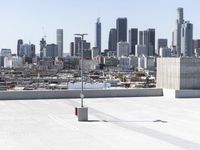 a man with black jacket skateboarding on cement outside of a building with city skyline in background