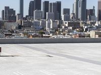 a man with black jacket skateboarding on cement outside of a building with city skyline in background