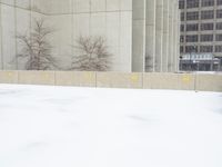 a parking meter sitting in the snow near buildings, looking toward the sidewalk area with trees