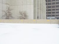 a parking meter sitting in the snow near buildings, looking toward the sidewalk area with trees