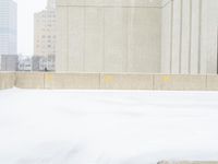 a parking meter sitting in the snow near buildings, looking toward the sidewalk area with trees