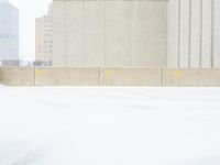 a parking meter sitting in the snow near buildings, looking toward the sidewalk area with trees