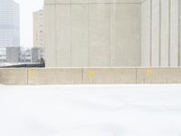 a parking meter sitting in the snow near buildings, looking toward the sidewalk area with trees