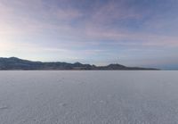 the snow is moving over the ground in the middle of the desert with mountain ranges