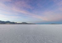 the snow is moving over the ground in the middle of the desert with mountain ranges