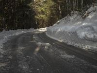 snow piled up on the side of a road next to a wooded area with trees in the background