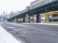 there is a yellow tram crossing a street with a bridge in the background while cars pass by