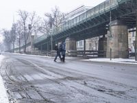 a snow covered street with traffic next to bridge and building overpasss on the left