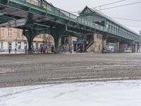 a street with several people on bicycles parked under a bridge near a snowy sidewalk on a cold winter day