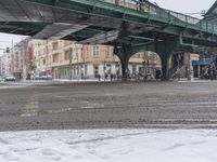 a street with several people on bicycles parked under a bridge near a snowy sidewalk on a cold winter day