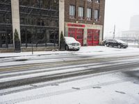 two cars driving through the snow on a snowy day in front of an old brick building