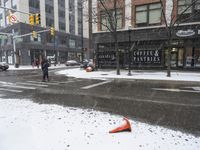 traffic cones near buildings in a downtown area on a winter day with snowflakes on the ground