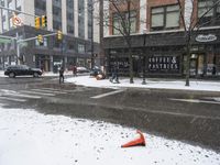 traffic cones near buildings in a downtown area on a winter day with snowflakes on the ground