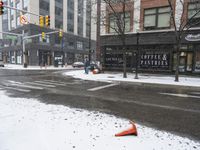 traffic cones near buildings in a downtown area on a winter day with snowflakes on the ground