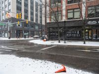 traffic cones near buildings in a downtown area on a winter day with snowflakes on the ground