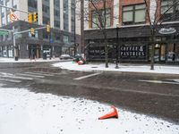 traffic cones near buildings in a downtown area on a winter day with snowflakes on the ground