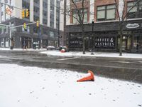 traffic cones near buildings in a downtown area on a winter day with snowflakes on the ground