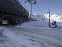 there are people riding on the ski lift and snowbanks below it and a large tunnel under a bridge