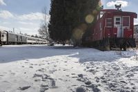 a red caboose and train cars parked near a tree and a snow covered trail