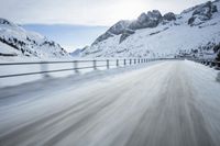 there is an extreme time exposure of snow traveling on this snowy road with mountains in the background