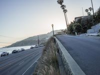 a street with cars driving down the road and hills in the background is a light house and blue ocean