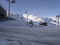 a snow covered parking lot surrounded by mountains in the distance and people climbing up, and ski lifts and ski lifts above