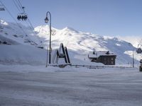 a snow covered parking lot surrounded by mountains in the distance and people climbing up, and ski lifts and ski lifts above