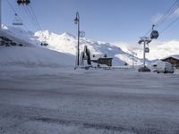 a snow covered parking lot surrounded by mountains in the distance and people climbing up, and ski lifts and ski lifts above