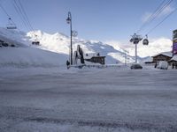 a snow covered parking lot surrounded by mountains in the distance and people climbing up, and ski lifts and ski lifts above