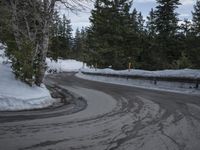 an empty asphalt road next to evergreen trees with snow on the ground and a sign warning of a closed off