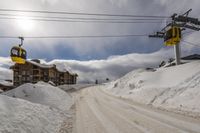 a yellow gondola is in the sky above a snowy mountain side road with snow drifts on it