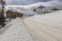 a yellow gondola is in the sky above a snowy mountain side road with snow drifts on it