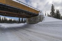 an overpass bridge that leads to the top of the snowy hill near an unfinished road