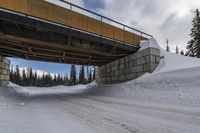 an overpass bridge that leads to the top of the snowy hill near an unfinished road