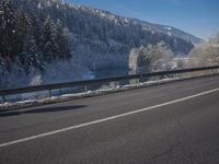 a large car driving on the highway in front of a snowy forest covered hillsides