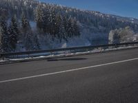 a large car driving on the highway in front of a snowy forest covered hillsides