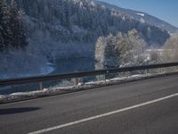 a large car driving on the highway in front of a snowy forest covered hillsides