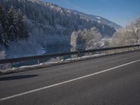 a large car driving on the highway in front of a snowy forest covered hillsides