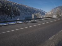 a large car driving on the highway in front of a snowy forest covered hillsides